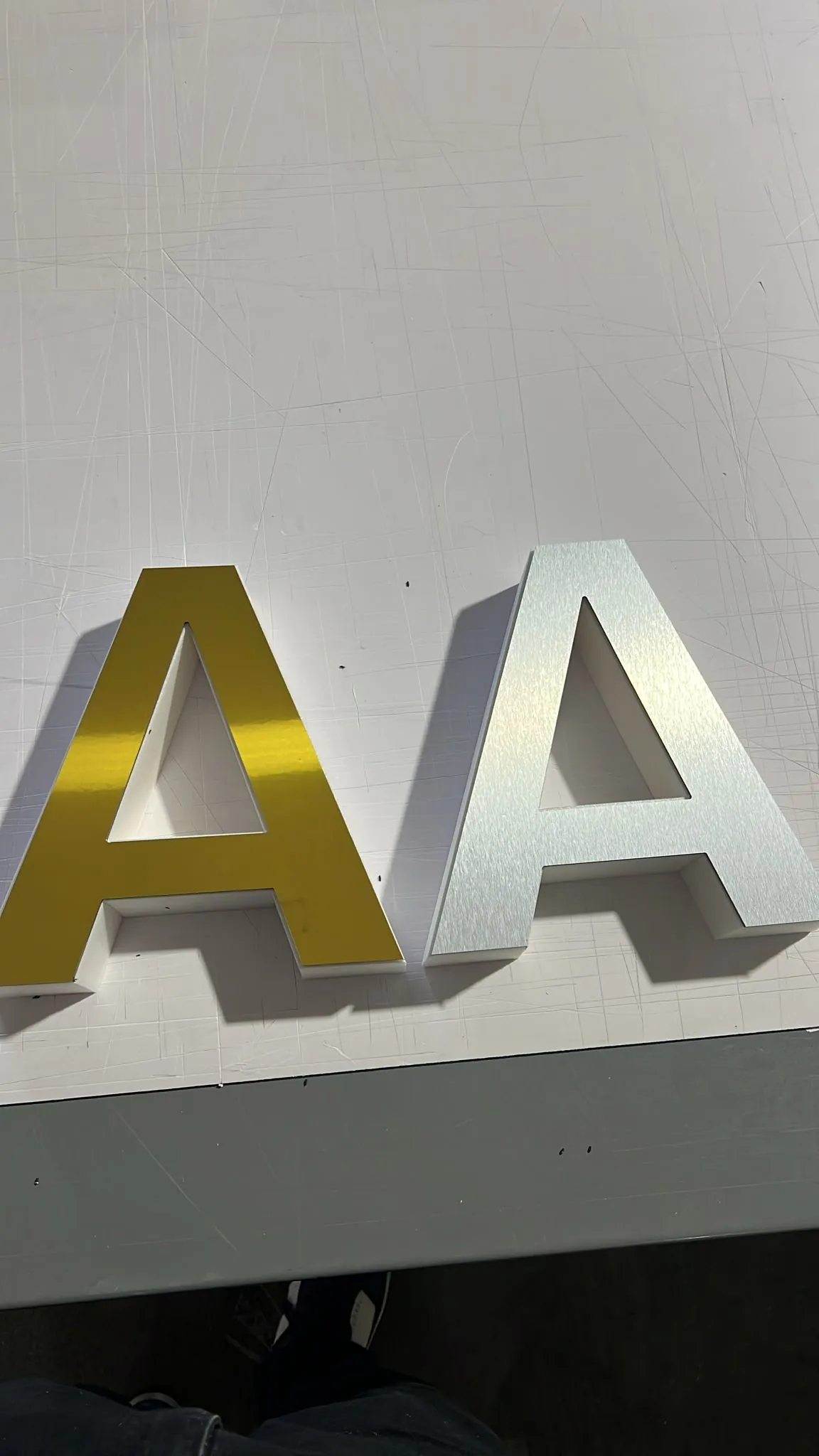 Two 3D letter samples on a work table, gold mirror and brushed aluminum